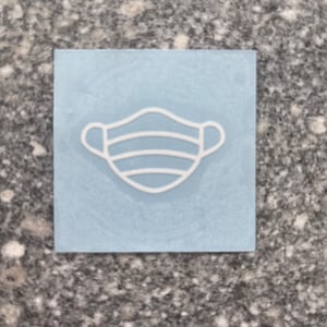 May include: A blue square sticker with a white outline of a face mask. The mask has three horizontal lines.