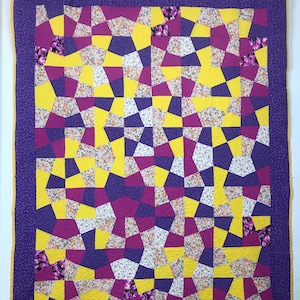 K&ouml;nnte beinhalten: Eine lila und gelbe Steppdecke mit geometrischem Muster. Die Steppdecke besteht aus verschiedenen Stoffen mit Blumendrucken.