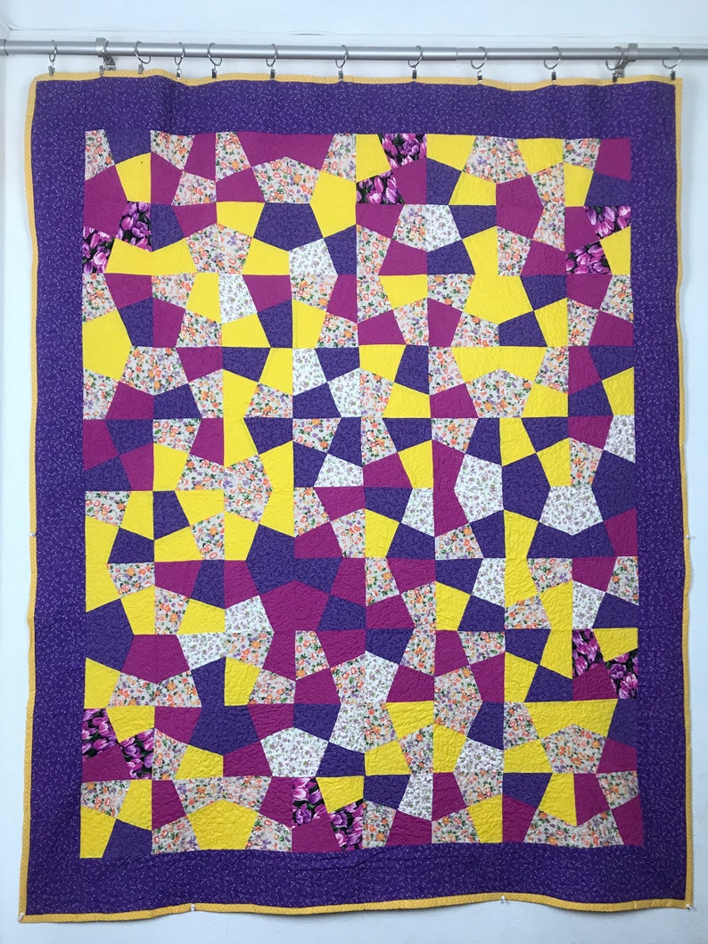 K&ouml;nnte beinhalten: Eine lila und gelbe Steppdecke mit geometrischem Muster. Die Steppdecke besteht aus verschiedenen Stoffen mit Blumendrucken.