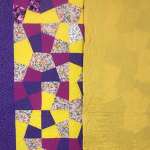 K&ouml;nnte beinhalten: Eine Steppdecke mit Patchwork-Muster aus gelbem, violettem und rosafarbenem Blumenstoff. Die Steppdecke besteht aus geometrischen Formen und ist mit einem einfarbigen gelben Stoff gef&uuml;ttert.