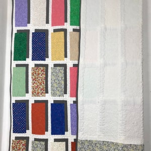 May include: A patchwork quilt with a variety of colorful fabrics and patterns. The quilt is hung on a rod and has a white backing.