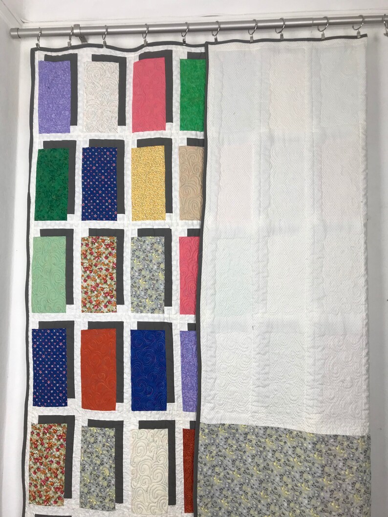 May include: A patchwork quilt with a variety of colorful fabrics and patterns. The quilt is hung on a rod and has a white backing.