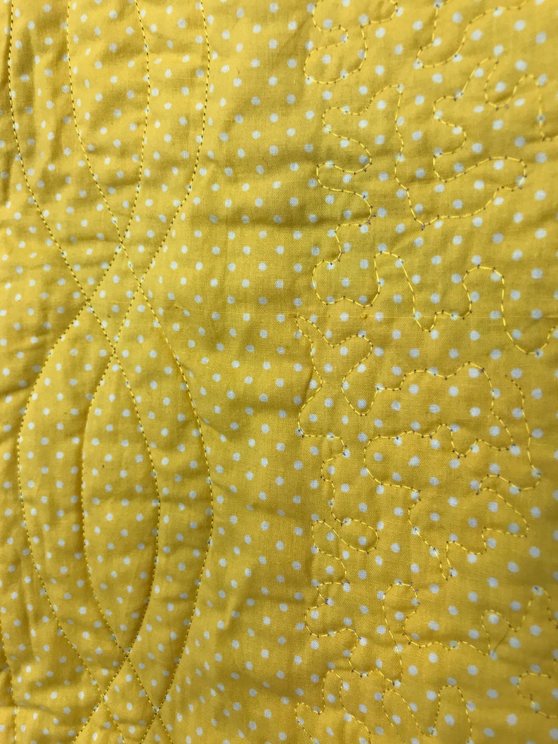 K&ouml;nnte beinhalten: Gelber Stoff mit wei&szlig;en Punkten und einem gesteppten Muster. Das Steppmuster zeigt eine Reihe von geschwungenen Linien und kleinen, abgerundeten Formen.