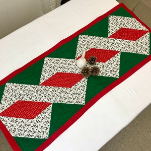 Peut inclure: Un chemin de table matelassé vert et rouge avec un motif en losanges blanc et rouge. Le chemin de table est bordé d'une bordure rouge et présente un imprimé floral blanc et vert.