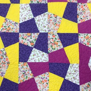 K&ouml;nnte beinhalten: Eine Steppdecke aus lila, gelbem und wei&szlig;em Stoff mit einem Blumenmuster. Die Steppdecke besteht aus vielen verschiedenen Formen und Gr&ouml;&szlig;en von Stoff.