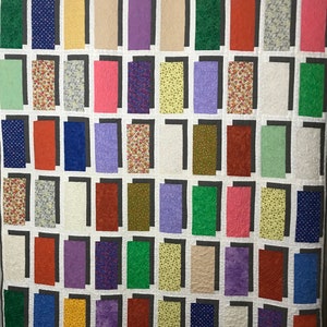 Può includere: Una trapunta con un design a patchwork che presenta una varietà di colori e motivi. La trapunta è composta da quadrati e rettangoli, ognuno con un tessuto diverso. I colori includono rosso, blu, verde, giallo, viola e bianco. I motivi includono stampe floreali, pois e disegni geometrici.