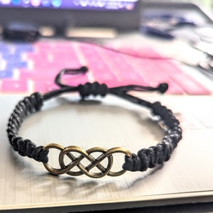 May include: A black braided cord bracelet with a gold infinity symbol charm.