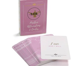Puede incluir: Una caja rosa con un diseño de lámpara dorada y el texto "The LOA Box" y "Positive Affirmations & Quotes". La caja contiene una pila de tarjetas rosas con diseños florales blancos y texto blanco. Una tarjeta es visible con el texto "I can AND I WILL" y "The LOA Box".