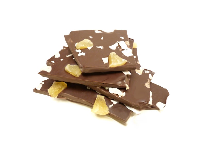 May include: Dark chocolate bark with pieces of candied ginger and coconut flakes. The chocolate is broken into irregular pieces and stacked on a white background. The ginger is a light yellow color.