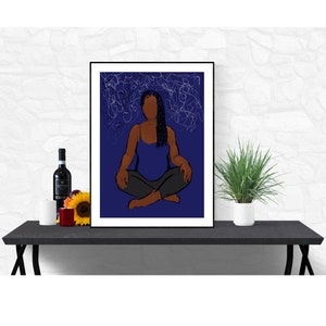 Könnte beinhalten: Ein Kunstdruck mit einer sitzenden Person in einem blauen Tanktop und grauer Hose vor einem dunkelblauen Hintergrund mit weißen Kritzeln. Das Kunstwerk ist schwarz gerahmt und auf einem schwarzen Tisch ausgestellt.