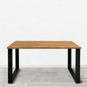 Può includere: Un tavolo in legno con una struttura in metallo nero. Il piano del tavolo è in legno naturale con una finitura marrone chiaro. Il tavolo è su un pavimento in legno grigio chiaro.