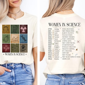 May include: A white t-shirt featuring a graphic of a grid of nine squares, each containing a different scientific image. The squares are in a vintage style with a brown and beige colour scheme. The text "WOMEN IN SCIENCE" is printed below the grid. The back of the shirt has a list of women in science and their contributions, with the years they made their discoveries.