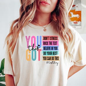 Peut inclure: Un t-shirt blanc avec un graphique coloré qui dit "You got this" avec le texte "Don't stress, Rock the test, Believe in you, Do your best, You can do this #testday" dans un schéma de couleurs arc-en-ciel.