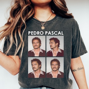 Peut inclure: Un t-shirt gris foncé à l'aspect délavé avec un collage de photos de Pedro Pascal. Le texte "PEDRO PASCAL" est imprimé en blanc au-dessus du collage.