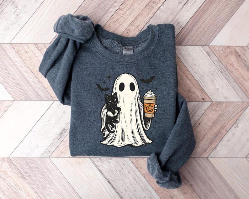 May include: A dark blue sweatshirt with a Halloween graphic. The design features a ghost holding a black cat and a pumpkin spice latte. Two bats and stars are also included. The sweatshirt is made of a soft material.