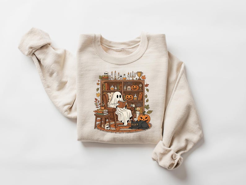 Peut inclure: Sweat-shirt cr&egrave;me avec un motif sur le th&egrave;me d'Halloween. Le dessin montre un fant&ocirc;me lisant dans un cadre confortable avec une biblioth&egrave;que, des citrouilles et un chat noir. Le sweat-shirt a des manches longues et un col rond.