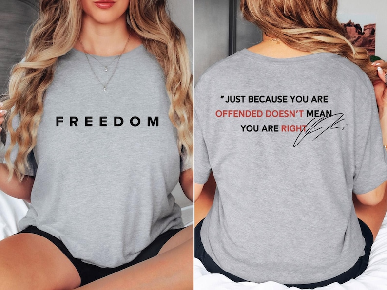 May include: A light gray t-shirt with the word "FREEDOM" printed in black on the front. The back of the shirt features the quote "JUST BECAUSE YOU ARE OFFENDED DOESN'T MEAN YOU ARE RIGHT" in black and red.