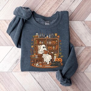 Peut inclure: Un sweat-shirt bleu marine avec un motif d'Halloween. Le dessin repr&eacute;sente un fant&ocirc;me lisant dans un fauteuil, avec des citrouilles, des bougies et un chat noir. Le sweat-shirt est fait d'une mati&egrave;re douce.