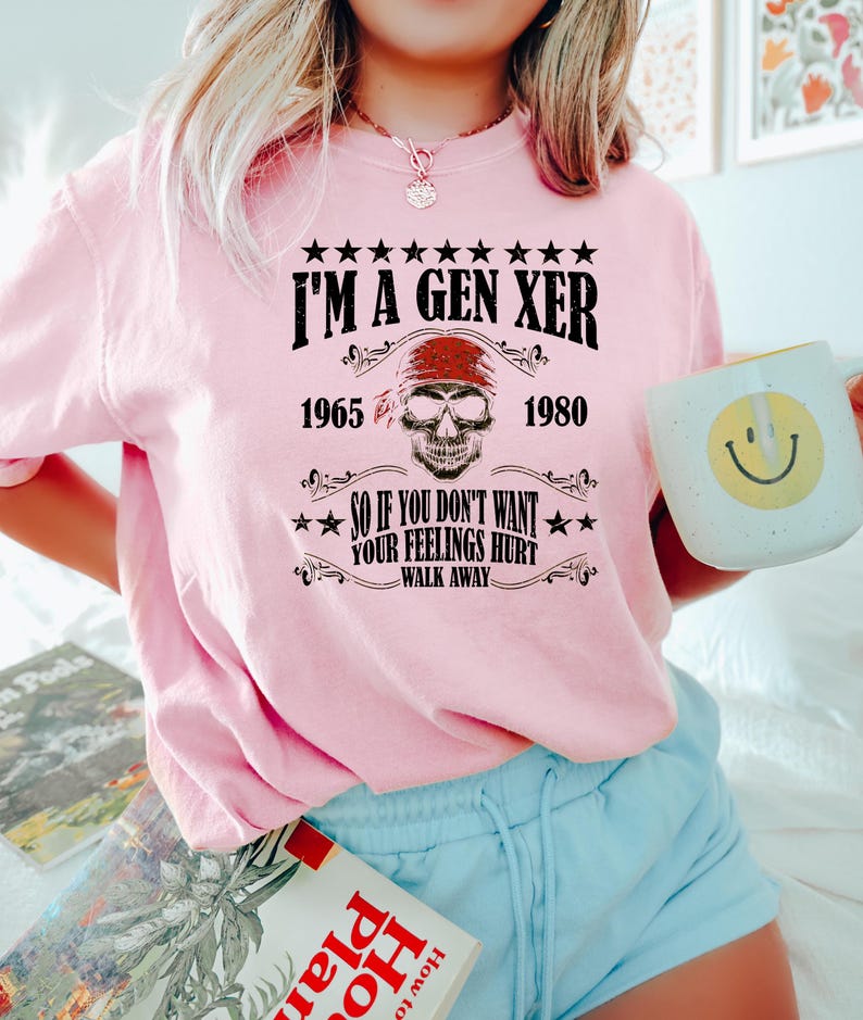 Op de afbeelding: Roze T-shirt met een zwarte afbeelding met de tekst "I'm a Gen Xer 1965 - 1980" en "So if you don't want your feelings hurt - walk away". De afbeelding bevat ook een schedel met een rode bandana.