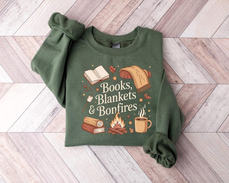 May include: Green sweatshirt with the text "Books, Blankets & Bonfires" and illustrations of a book, blanket, bonfire, and mug. The sweatshirt is a solid green color.