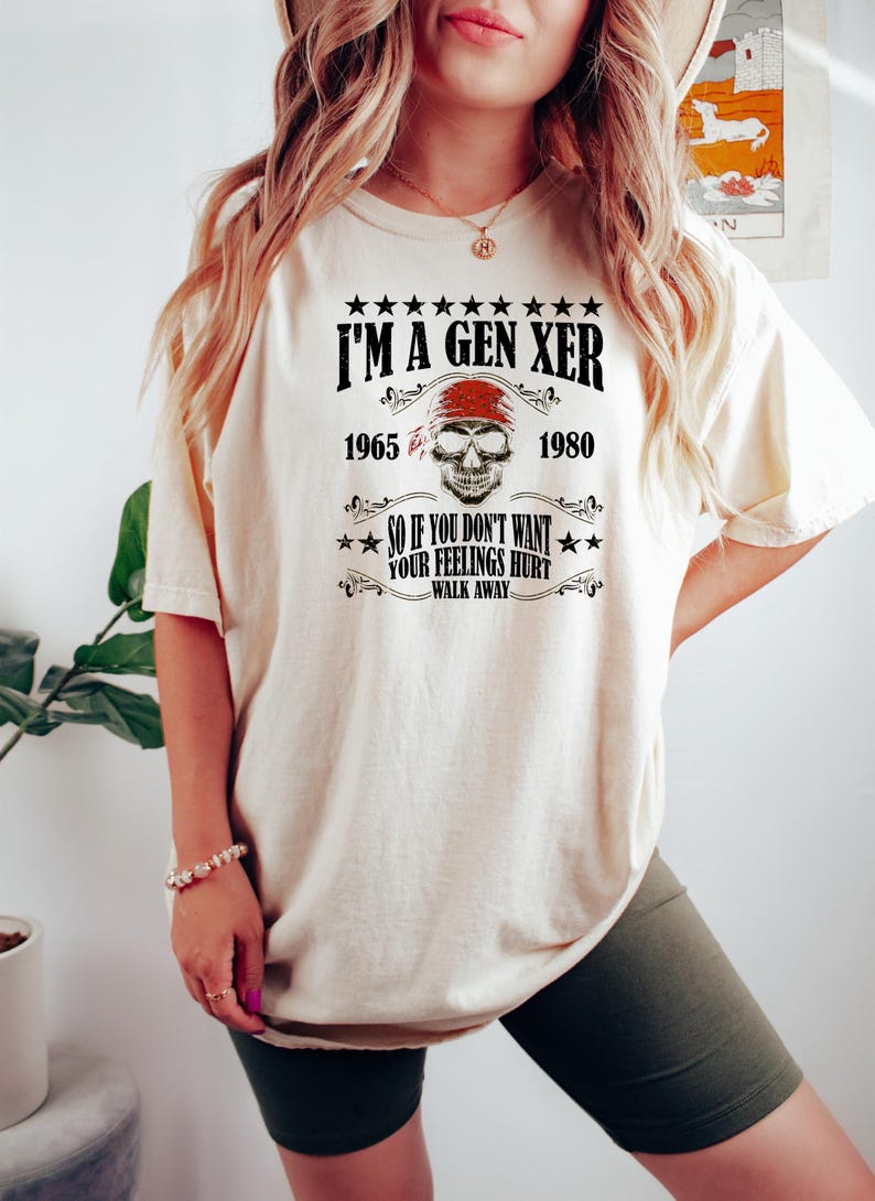 Op de afbeelding: Een wit T-shirt met een zwarte grafische print die "I'm a Gen Xer" zegt met een schedel en gekruiste beenderen en de jaren 1965 en 1980. De tekst onder de schedel zegt "So if you don't want your feelings hurt walk away."