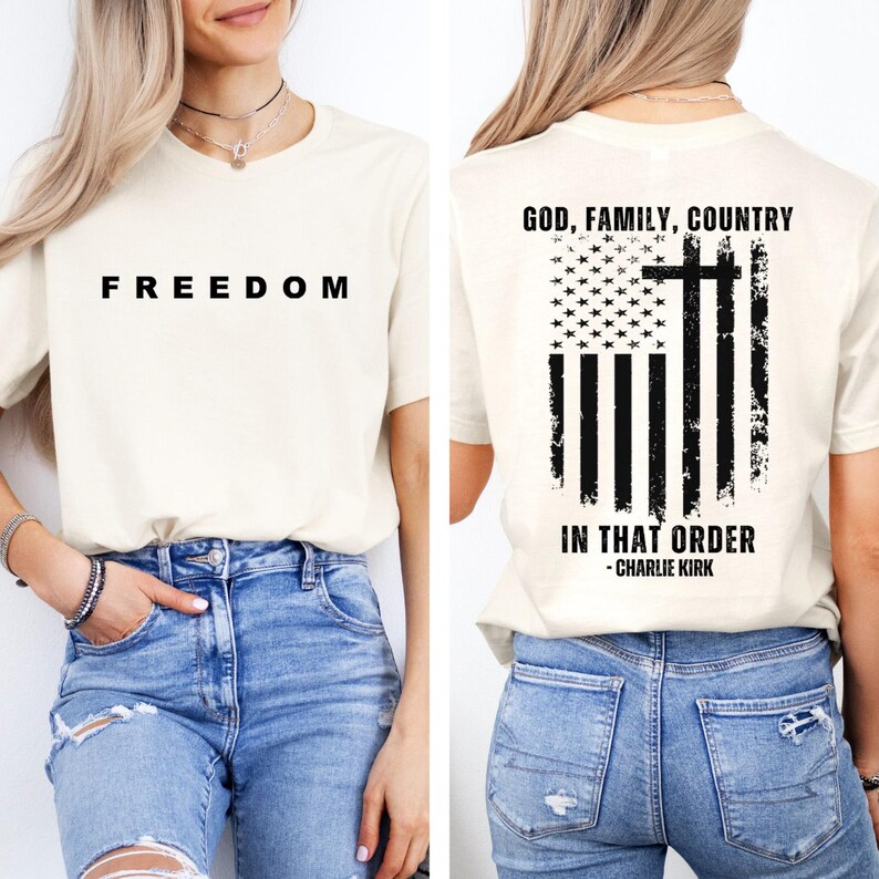 May include: Cream-colored t-shirt with the word "FREEDOM" printed in black on the front. The back of the shirt features a distressed American flag design with a cross and the text "GOD, FAMILY, COUNTRY IN THAT ORDER - CHARLIE KIRK."
