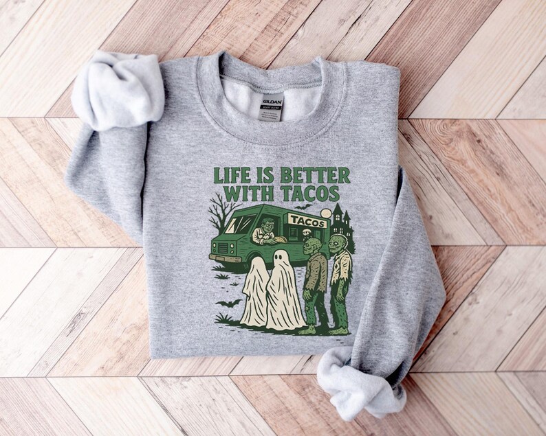 May include: A heather gray sweatshirt with a crew neck. The front features a green taco truck graphic with the text "LIFE IS BETTER WITH TACOS". Ghosts and zombies are also in the graphic.
