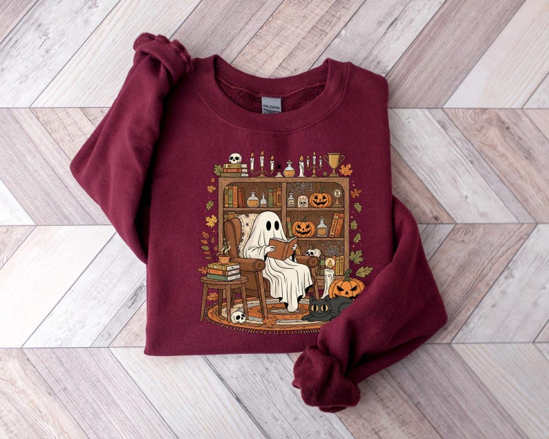 Peut inclure: Sweat-shirt bordeaux avec un motif sur le th&egrave;me d'Halloween. Le motif repr&eacute;sente un fant&ocirc;me lisant dans une biblioth&egrave;que confortable avec des citrouilles, des bougies et un chat noir. Le sweat-shirt est en mati&egrave;re douce.