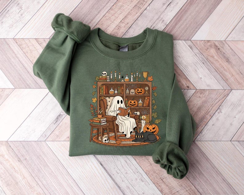Peut inclure: Sweat-shirt vert avec un fant&ocirc;me lisant un livre dans une biblioth&egrave;que. Le motif comprend une &eacute;tag&egrave;re avec des citrouilles, des bougies et un chat noir. Le sweat-shirt a des manches longues et un col rond.