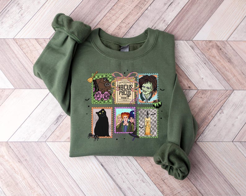 Puede incluir: Una sudadera verde oliva con un gr&aacute;fico colorido de sellos postales con im&aacute;genes y texto de la pel&iacute;cula "Hocus Pocus". Los sellos incluyen un gato negro, un caballo y las hermanas Sanderson.