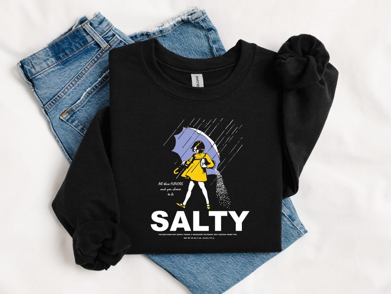 May include: Black sweatshirt with a graphic of a person under a blue umbrella, with the word "SALTY" in white. The person is wearing a yellow coat and the text "All the flavors and you choose to be" is above the word "SALTY".