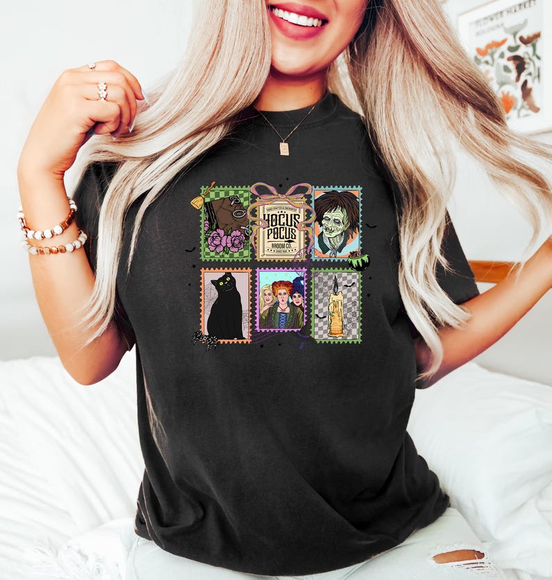 Puede incluir: Camiseta negra con un collage de im&aacute;genes estilo sello postal. Las im&aacute;genes incluyen un gato negro, un zombi, una escoba y el texto "Hocus Pocus". La camiseta tiene cuello redondo y mangas cortas.