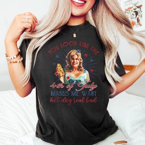 May include: A black t-shirt with a graphic of a woman holding a hot dog. The text on the shirt reads "You look like the 4th of July makes me want hot dog real bad."