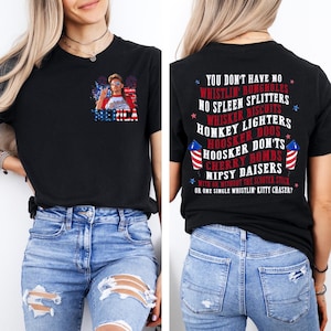 Pode incluir: Camiseta preta com um gr&aacute;fico de uma pessoa usando &oacute;culos de sol e a palavra "AMERICA" em vermelho, branco e azul. A parte de tr&aacute;s da camisa tem uma lista de frases em texto branco, incluindo "WHISTLIN' BUNGHOLES" e "CHERRY BOMBS".