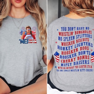 Pode incluir: Camiseta cinza claro com um design patri&oacute;tico. A frente apresenta uma pessoa com &oacute;culos de sol e a palavra "MERICA". A parte de tr&aacute;s mostra texto patri&oacute;tico e fogos de artif&iacute;cio.