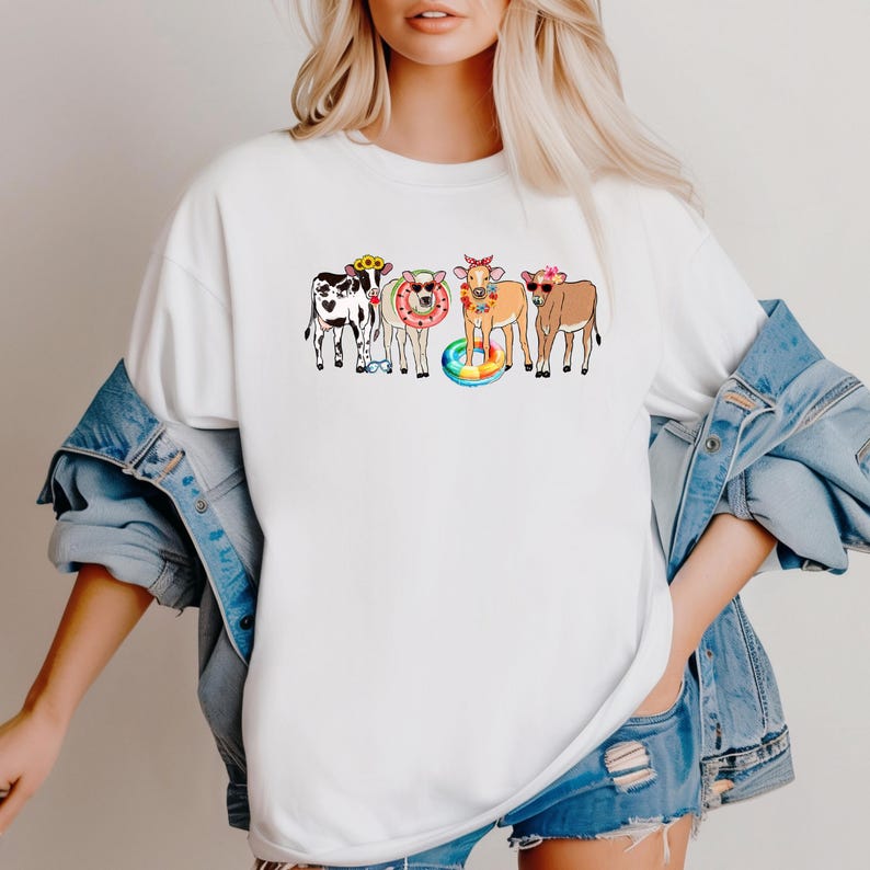 Pu&ograve; includere: T-shirt bianco con una grafica colorata di cinque mucche dei cartoni animati. Ogni mucca indossa occhiali da sole, fasce floreali e salvagenti, creando un'atmosfera estiva e divertente. Il design &egrave; giocoso e accattivante.