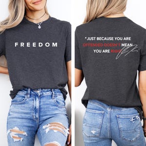 May include: Dark gray t-shirt with the word "FREEDOM" printed in white on the front. The back of the shirt features the quote "JUST BECAUSE YOU ARE OFFENDED DOESN'T MEAN YOU ARE RIGHT" in white and red.