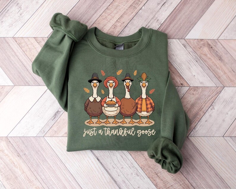Pu&ograve; includere: Felpa verde con una grafica di quattro oche dei cartoni animati con cappelli e abiti autunnali. Il testo "just a thankful goose" &egrave; sotto. La felpa &egrave; realizzata in un materiale morbido.