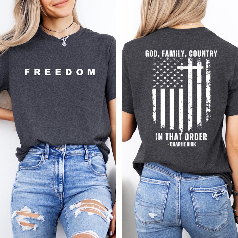 May include: Dark gray t-shirt with the word "FREEDOM" in white block letters on the front. The back of the shirt features an American flag design with a cross and the text "GOD, FAMILY, COUNTRY IN THAT ORDER - CHARLIE KIRK."