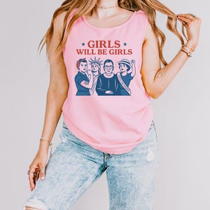 May include: Pink tank top with the text "GIRLS WILL BE GIRLS" and a graphic of four women. The graphic includes the Statue of Liberty and Ruth Bader Ginsburg. The tank top is sleeveless.