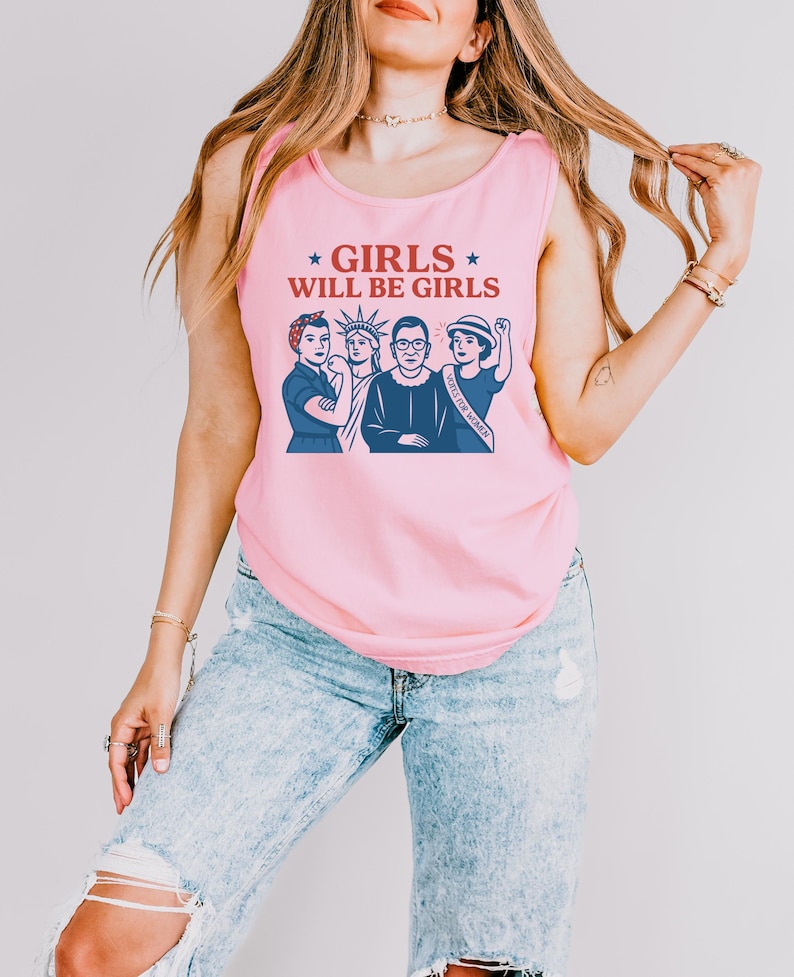 May include: Pink tank top with the text "GIRLS WILL BE GIRLS" and a graphic of four women. The graphic includes the Statue of Liberty and Ruth Bader Ginsburg. The tank top is sleeveless.