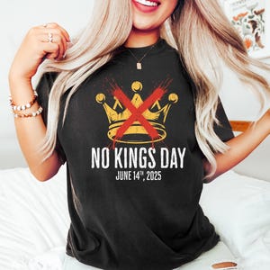 May include: Black t-shirt with a gold crown design crossed out in red, and the text "NO KINGS DAY JUNE 14TH, 2025". The shirt is a dark color and has a vintage look.