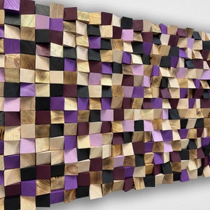 Op de afbeelding: Een wandkunstwerk bestaande uit houten blokken in verschillende kleuren, waaronder natuurlijke houttinten, zwart, paars en lavendel. De blokken zijn in een mozaïkpatroon gerangschikt, wat een textuur en driedimensionaal effect creëert. Geschikt voor interieurdecoratie.