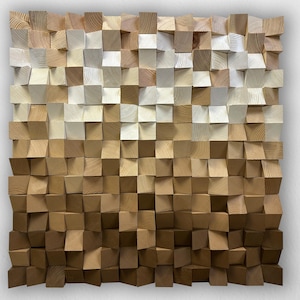 Può includere: Un'opera d'arte murale quadrata in legno composta da numerosi piccoli blocchi tagliati in modo irregolare. I blocchi cambiano colore, passando dal beige chiaro in alto al marrone scuro in basso, creando un effetto sfumato. La consistenza generale è ruvida e tridimensionale.