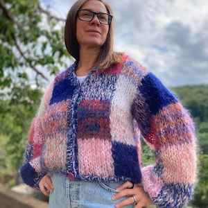 May include: A pink, blue and white patchwork cardigan with a button fastening. The cardigan has a relaxed fit and long sleeves.