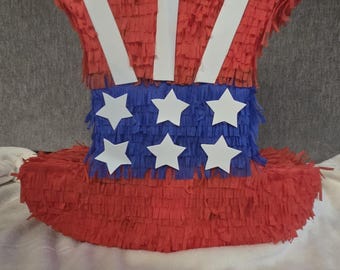 May include: A red, white, and blue Uncle Sam hat piñata. The hat features red fringe, white stripes, a blue band with white stars, and a wide brim. Perfect for patriotic celebrations and themed parties.