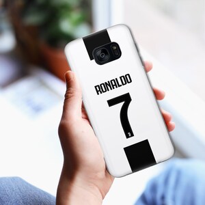 May include: White phone case with a black stripe down the side. The case has the name "RONALDO" and the number "7" printed on it in black.