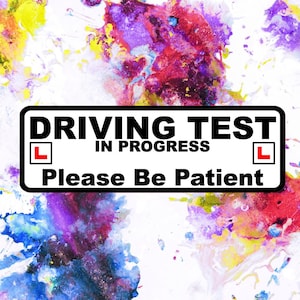 May include: A rectangular sign with the text "DRIVING TEST IN PROGRESS Please Be Patient" in black font. The sign has a white background with a black border and red "L" symbols. The background is a colorful abstract design.