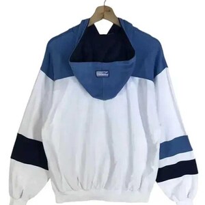 Puede incluir: Chaqueta con capucha blanca, azul y azul marino colgada de una percha de madera. La chaqueta tiene un dise&ntilde;o de bloques de color con capucha y mangas azules, cuerpo blanco y rayas azul marino y azules en las mangas.