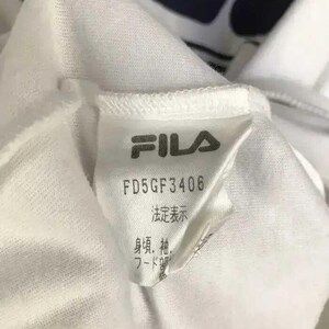 Puede incluir: Primer plano de una etiqueta de prenda blanca con el logotipo de FILA en gris. La etiqueta muestra el texto "FD5GF3406" y caracteres japoneses. La prenda parece estar hecha de una tela blanca suave.